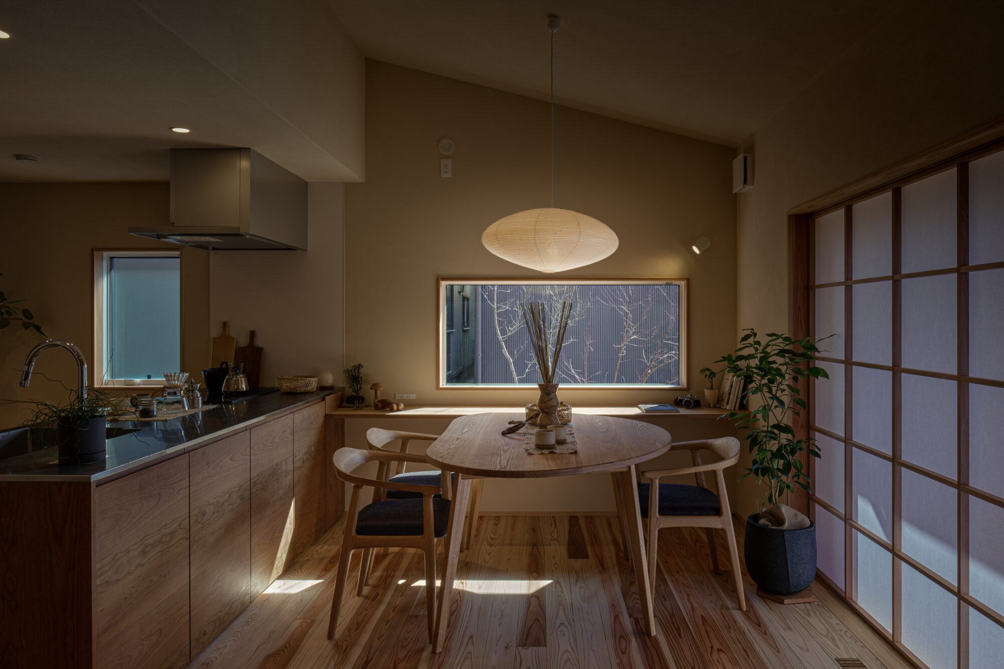 Warm kitchen and dining area with wooden table and chairs, a hanging paper lantern, and a grid-pattern sliding screen on the right.