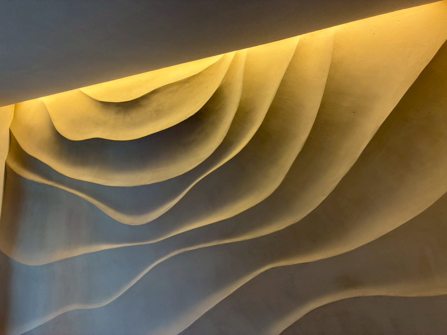 Abstract, wave-like concrete curves bathed in warm yellow light from above.