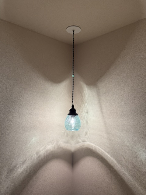 A blue glass pendant light hanging from the ceiling, lit and casting soft shadows on the beige walls.
