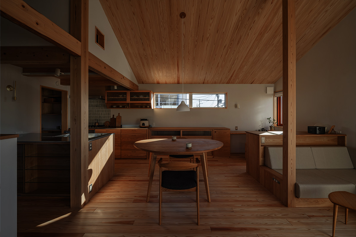 Warm wood-toned kitchen and dining area with a round table, built-in seating, and a vaulted wooden ceiling.
