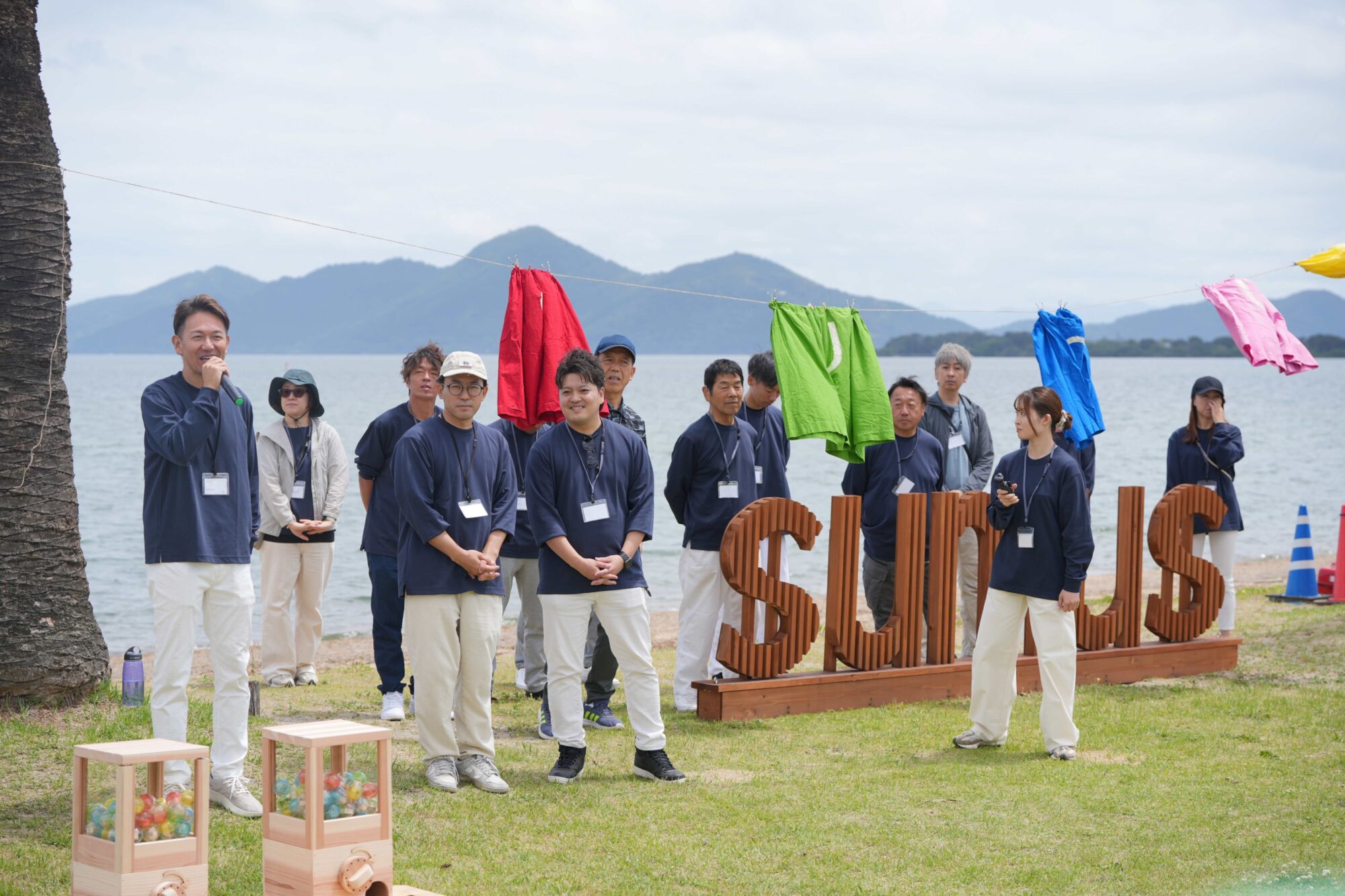 Team of people in navy outfits on a beach, with colorful clothes hanging on a line behind them by the water.