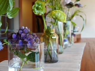 Row of glass vases with colorful flowers arranged along a light table indoors.