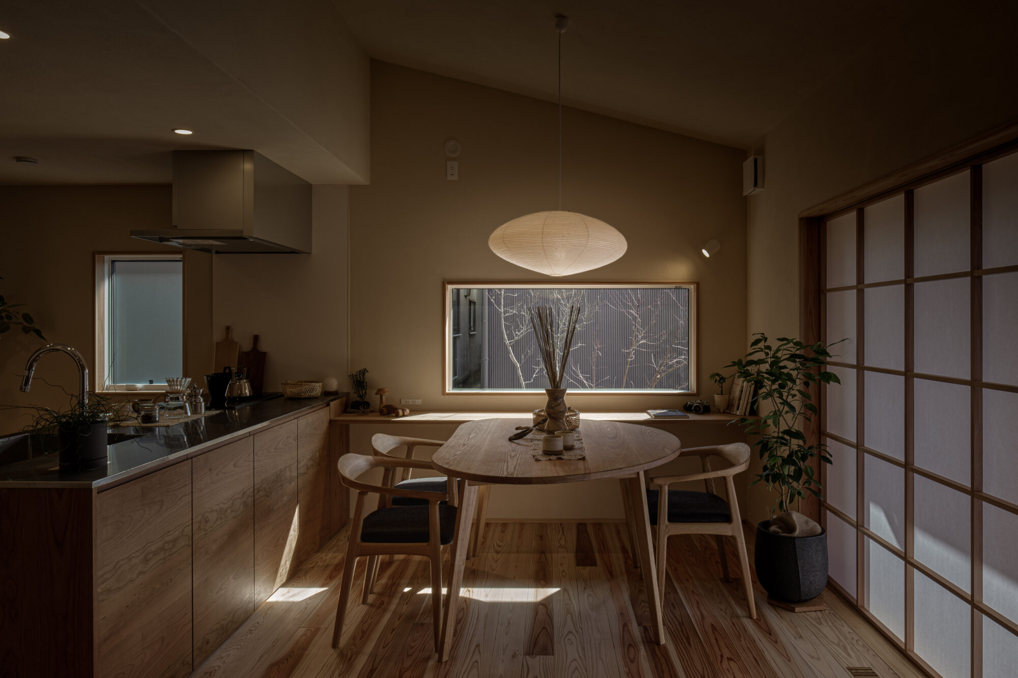 Cozy kitchen and dining area with a round wooden table, matching chairs, and a hanging paper pendant light in warm, earthy tones.
